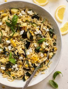 a bowl filled with rice and vegetables next to sliced lemons on a white surface