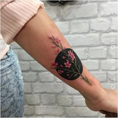 a woman's arm with a black and pink flower tattoo on the left forearm