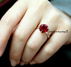 a woman's hand with a gold ring and a red gemstone stone on it