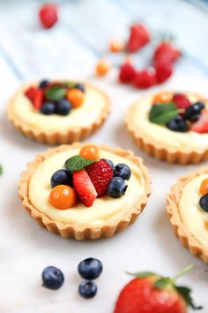 small pies with fruit on top are arranged on a white surface next to strawberries and blueberries