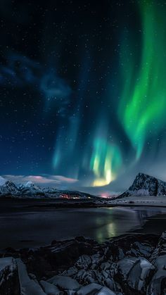 the northern lights shine brightly over snow covered mountains and water in this landscape photo taken at night