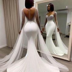 a woman in a wedding dress looking at herself in the mirror with her back to the camera