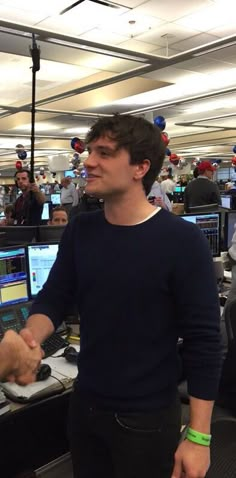 two men shaking hands in an office cubicle with many computers on the desks