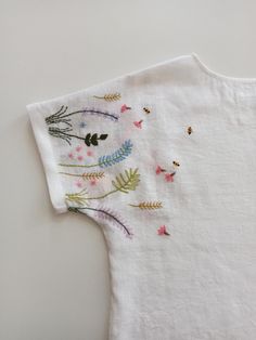 a white t - shirt with embroidered flowers and leaves on the front, sitting on a table