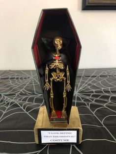 a gold and black skeleton figurine in a wooden box on a table with a plaque