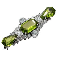 A spectacular early twentieth century brooch centered around an emerald cut peridot, surrounded by diamonds, and finished on either side with shield cut peridot. The central stone weighs approximately 10.5ct, and the combined weight of the two shield cut peridot is approximately 7.5ct. The 4 diamonds set along the 4 sides of the center peridot weigh approximately 2.5ct. total weight. The diamonds accenting the geometric design of the brooch weigh a total of approximately 1.66ct. Overall color of the diamonds is J color, and overall clarity is VS2-SI2. Measuring 2 1/4 inches long, by 7/8 inch wide, it is noticeable, while being very tasteful. Gross weight 14 grams. Birthday Symbols, Peridot Brooch, 1920s Jewelry, Sea House, Fun Jewelry, Stone Design, August Birth Stone, Antique Art Deco, High Jewelry