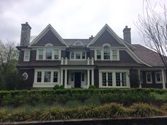 a large brown house with white trim and windows on the top floor, surrounded by hedges