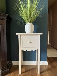 a white table with a potted plant on top of it next to a dresser