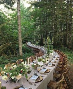 a long table is set up in the woods with place settings and flowers on it