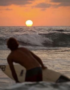 a man sitting on top of a surfboard next to the ocean at sunset or dawn