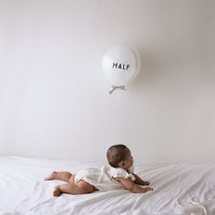 a baby sitting on a bed with a balloon attached to the wall