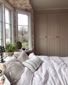 a bed with white sheets and pillows next to two windows