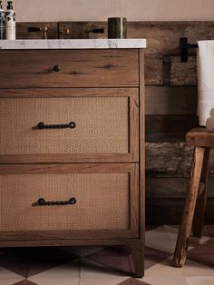 a bathroom vanity with two drawers next to a stool and towel on the counter top