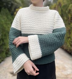 a woman wearing a green and white knitted sweater standing in front of some bushes