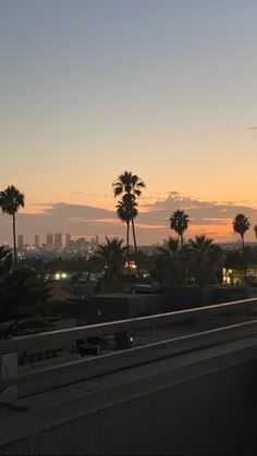 the sun is setting behind some palm trees on top of a hill in front of a cityscape