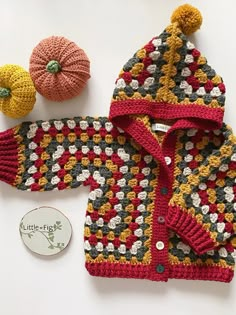 a crocheted sweater, hat and pumpkin on a white surface with a button