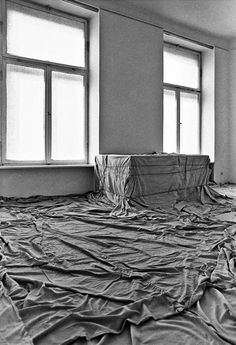 an empty room with sheets on the floor and windows in the wall, all covered by tarp