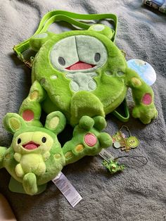 two green stuffed animals sitting on top of a bed next to a purse and keychain