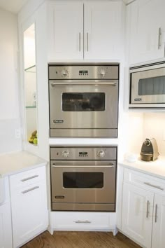 two ovens in a kitchen with white cabinets and wood flooring on the walls