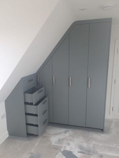 an empty room with grey cabinets and drawers in the corner, next to a slanted wall