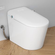 a white toilet sitting on top of a wooden floor next to a wall mounted faucet