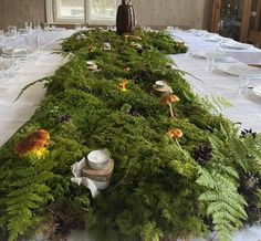 the table is covered with green moss and white linens, surrounded by glassware