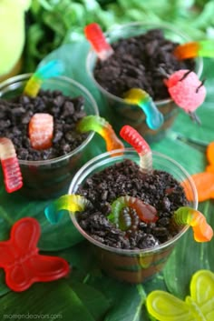 three small cups filled with dirt and gummy bears on top of green leafy leaves