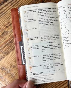 a person holding an open book on top of a wooden table with writing in it