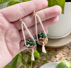 a person is holding two small plants in their palm tree shaped planter earrings with tassels hanging from them