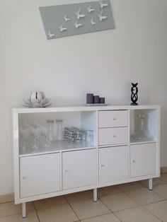 a white cabinet with birds on the wall above it and glassware in front of it