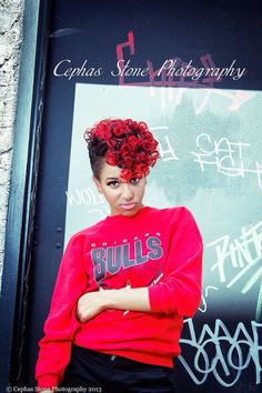 a woman with red curly hair standing in front of a graffiti covered wall and posing for the camera