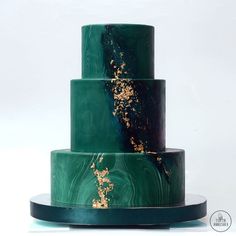 a three tiered green cake with gold leaf decorations on it's sides and bottom