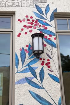 a lamp on the side of a building with blue leaves and red berries painted on it