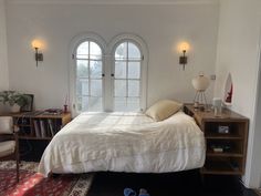 a bedroom with a bed, two windows and a rug on the floor in front of it