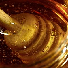 honey in a glass jar with a wooden spoon sticking out of the top and bubbles on the bottom