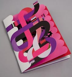 an open book with pink, purple and red designs on the front cover sitting on top of a gray surface