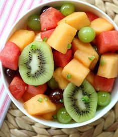 a white bowl filled with sliced fruit on top of a woven table cloth next to a fork