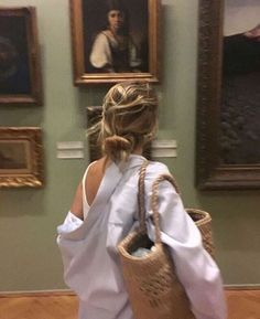 a woman in white dress carrying a large woven basket on her back while walking through an art gallery