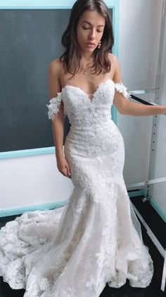 a woman in a white wedding dress leaning against a chalkboard with her hand on the wall