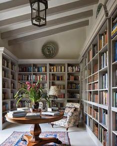 a room filled with lots of books and furniture next to a lamp hanging from the ceiling