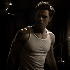 a man standing in the dark wearing a tank top