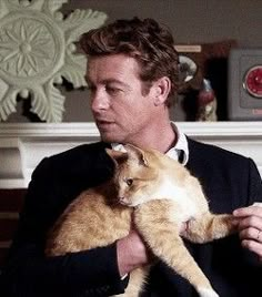 a man holding an orange and white cat in his lap while wearing a black suit