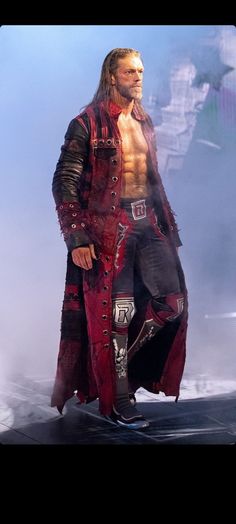 a man dressed in red and black standing on top of a stage with his shirt open