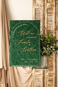 a green and gold wedding sign hanging from the side of a wooden door next to a potted plant