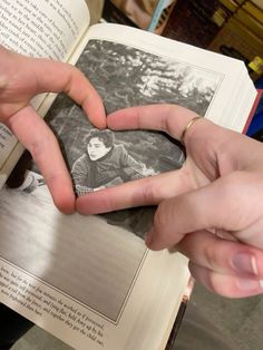 two hands holding an open book with a heart shaped photo in the middle and another hand making a heart shape