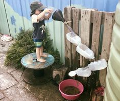 a little boy standing on top of a wooden table next to a bucket filled with water