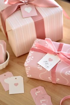 pink gift boxes with tags and ribbons on top of a wooden table next to other items