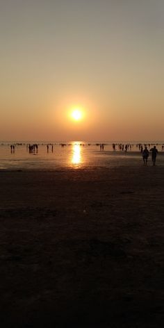 people are walking on the beach as the sun goes down in the distance behind them