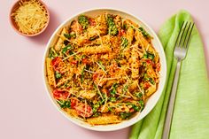 a white bowl filled with pasta and vegetables next to a green napkin on top of a pink surface