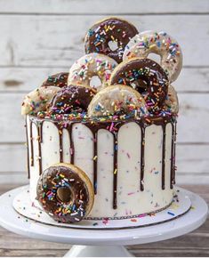 a white cake with chocolate frosting and sprinkles on top, topped with donuts